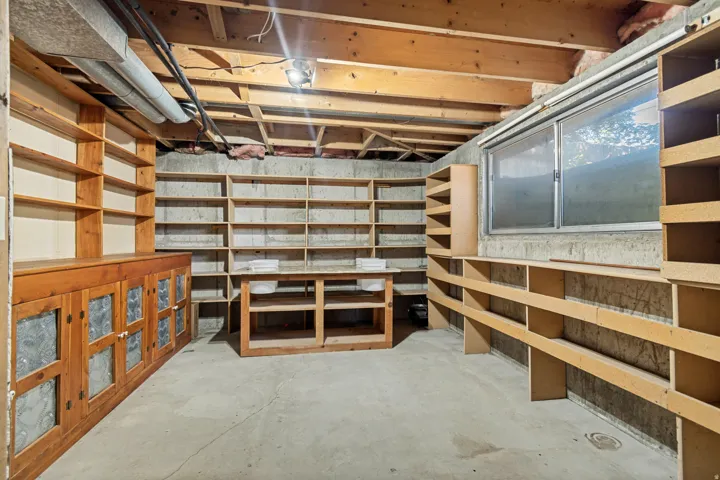 Exposed wood ceiling beams, concrete flooring, built-in wooden shelving, a built-in wooden cabinet with glass-paneled doors, and a window for natural light