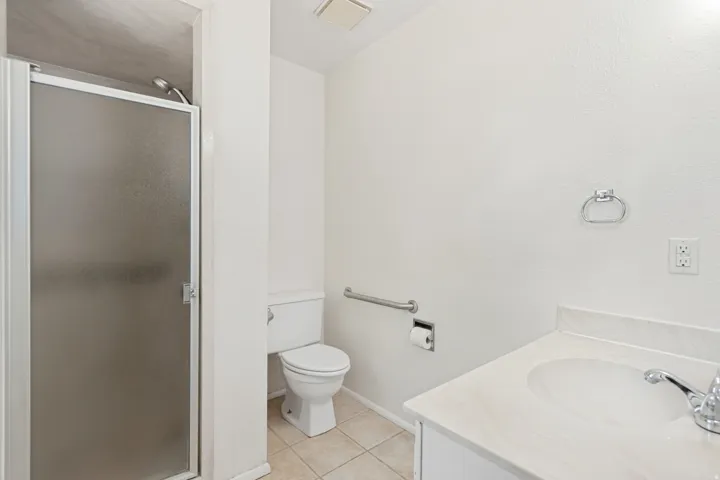 Bathroom featuring a shower with frosted glass enclosure, white vanity with integrated sink, chrome faucet, and grab bar