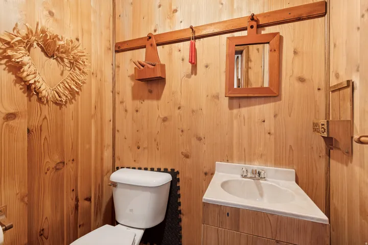 Tongue and groove wood paneling throughout, white toilet, white corner vanity with integrated sink, chrome faucet, and wood-finish cabinetry