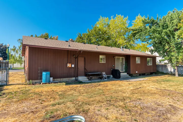 Brown siding exterior with a shingle roof, concrete patio, and mature trees
