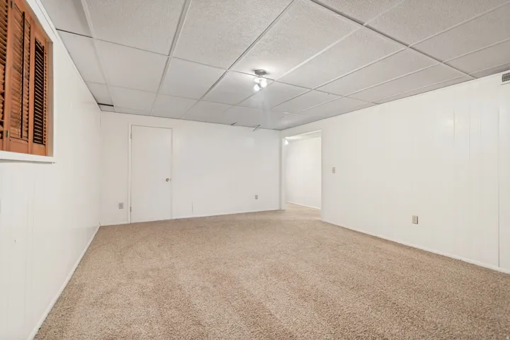 Carpeted flooring, white panel walls, and a drop ceiling with recessed lighting