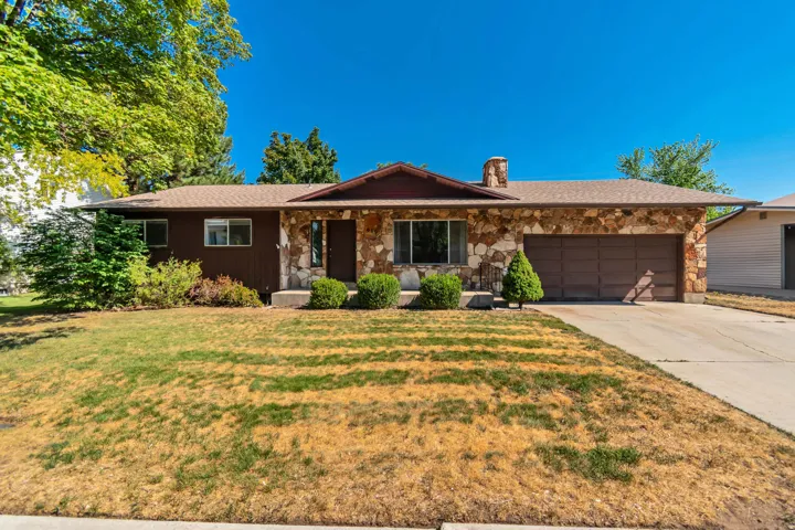 Stone façade, attached garage, concrete driveway, and mature landscaping