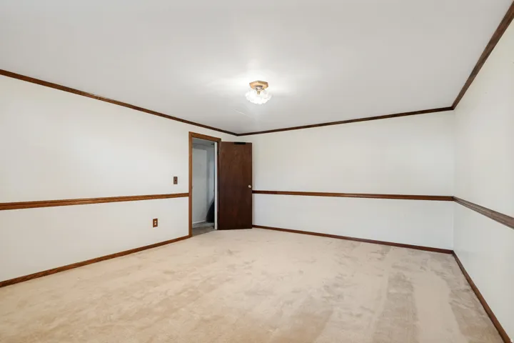Carpeted flooring, white walls, dark wood-finish trim, ceiling-mounted light fixture, and a solid wood-finish door
