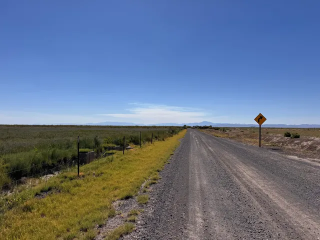 Expansive rural property featuring a long gravel driveway bordered by post-and-wire fencing, native grassland, and open acreage extending across the horizon under clear skies