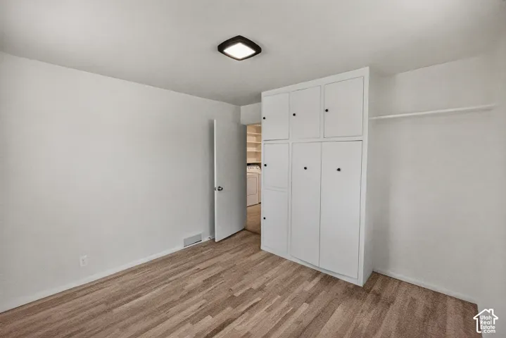 Wood-finish flooring, built-in white cabinetry with black hardware, white walls, and flush-mount ceiling light