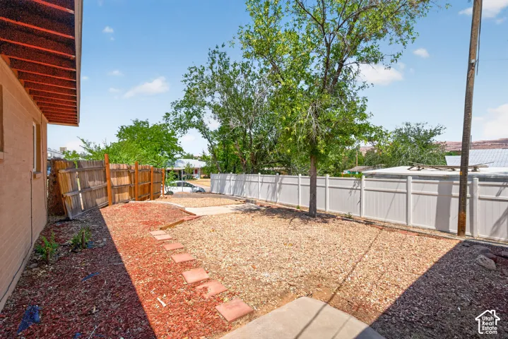 Fenced backyard featuring a large tree, stone ground cover, and a concrete patio section