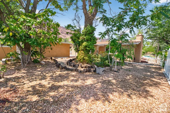 Exterior featuring a stucco finish, mature trees, a wood chip ground cover, a white picket fence, and a distant mountain backdrop