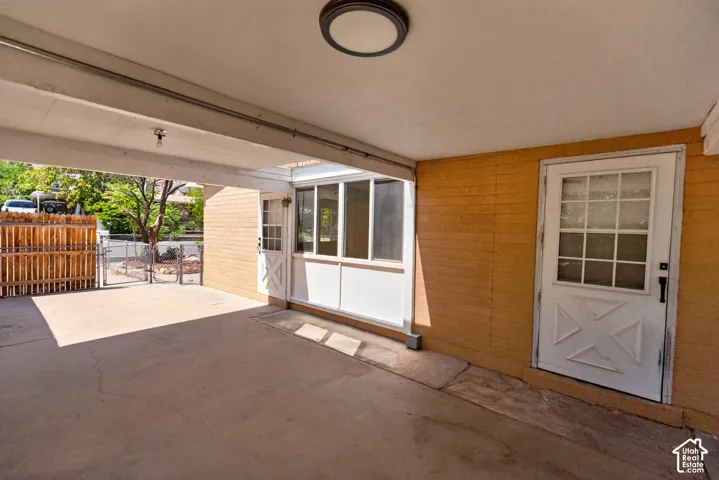 Covered carport with a concrete slab, exterior lighting, and a white paneled door