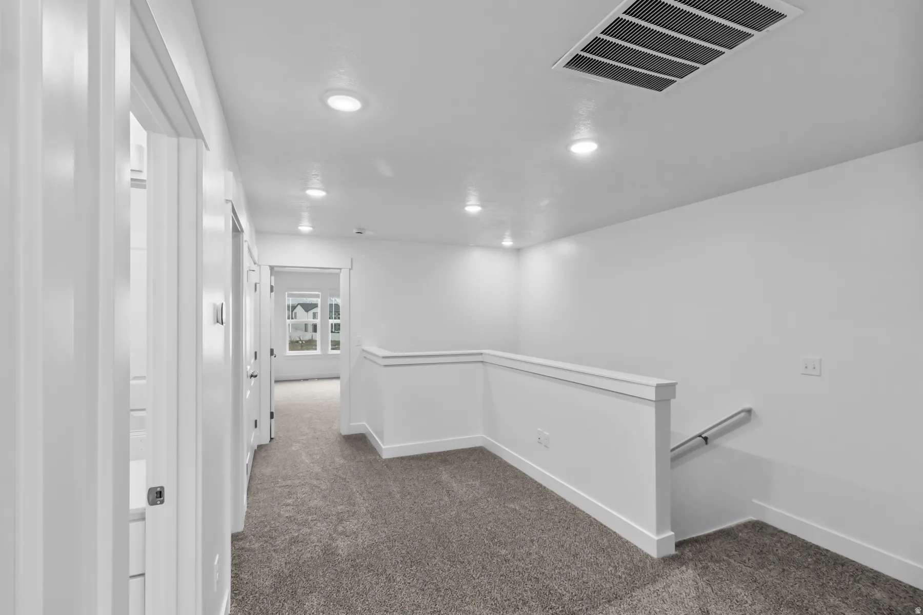 Carpeted hallway with white walls, recessed ceiling lighting, and white railings