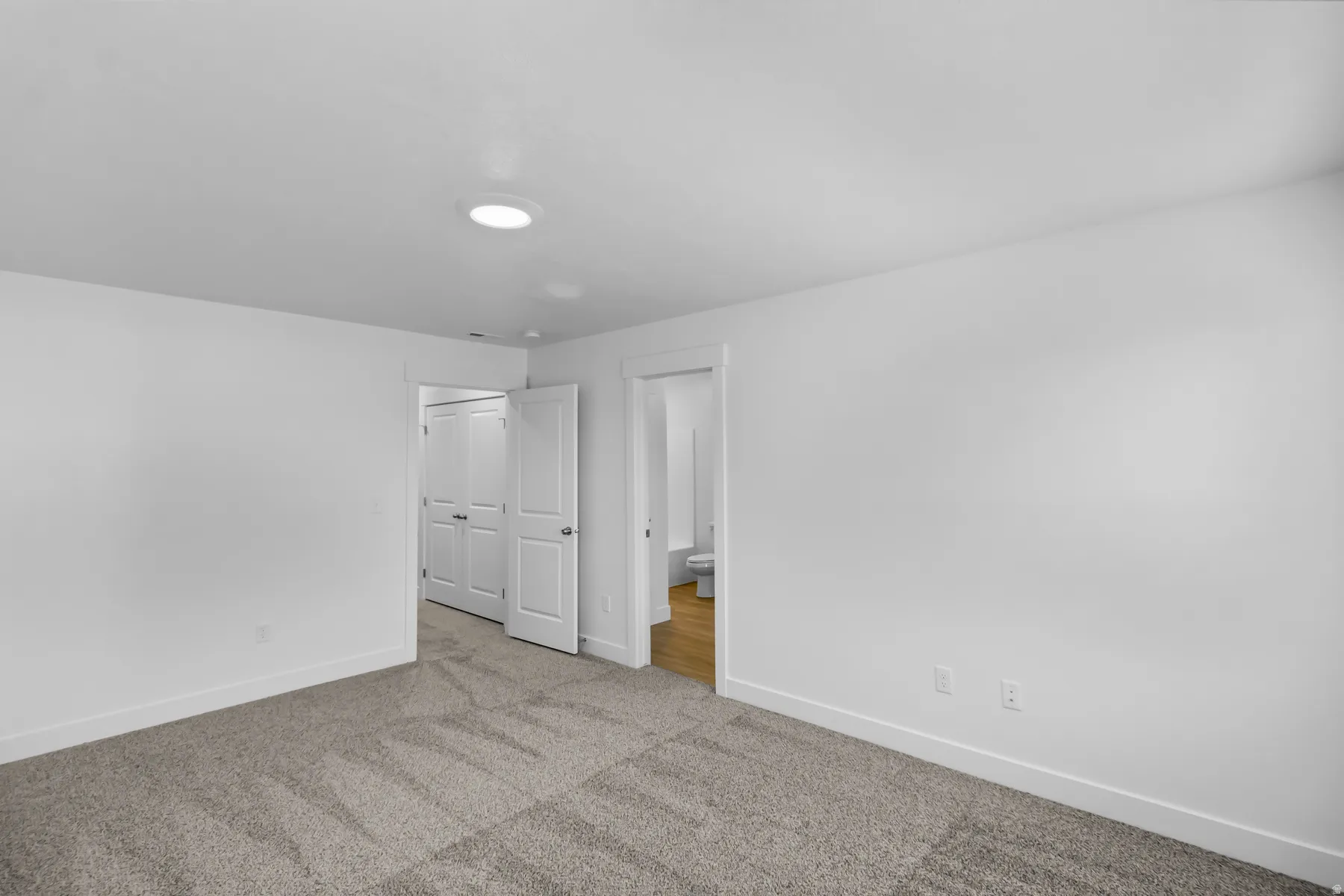 Recessed ceiling lighting, neutral carpeting, two-panel interior doors, and wood-finish flooring in the adjacent space