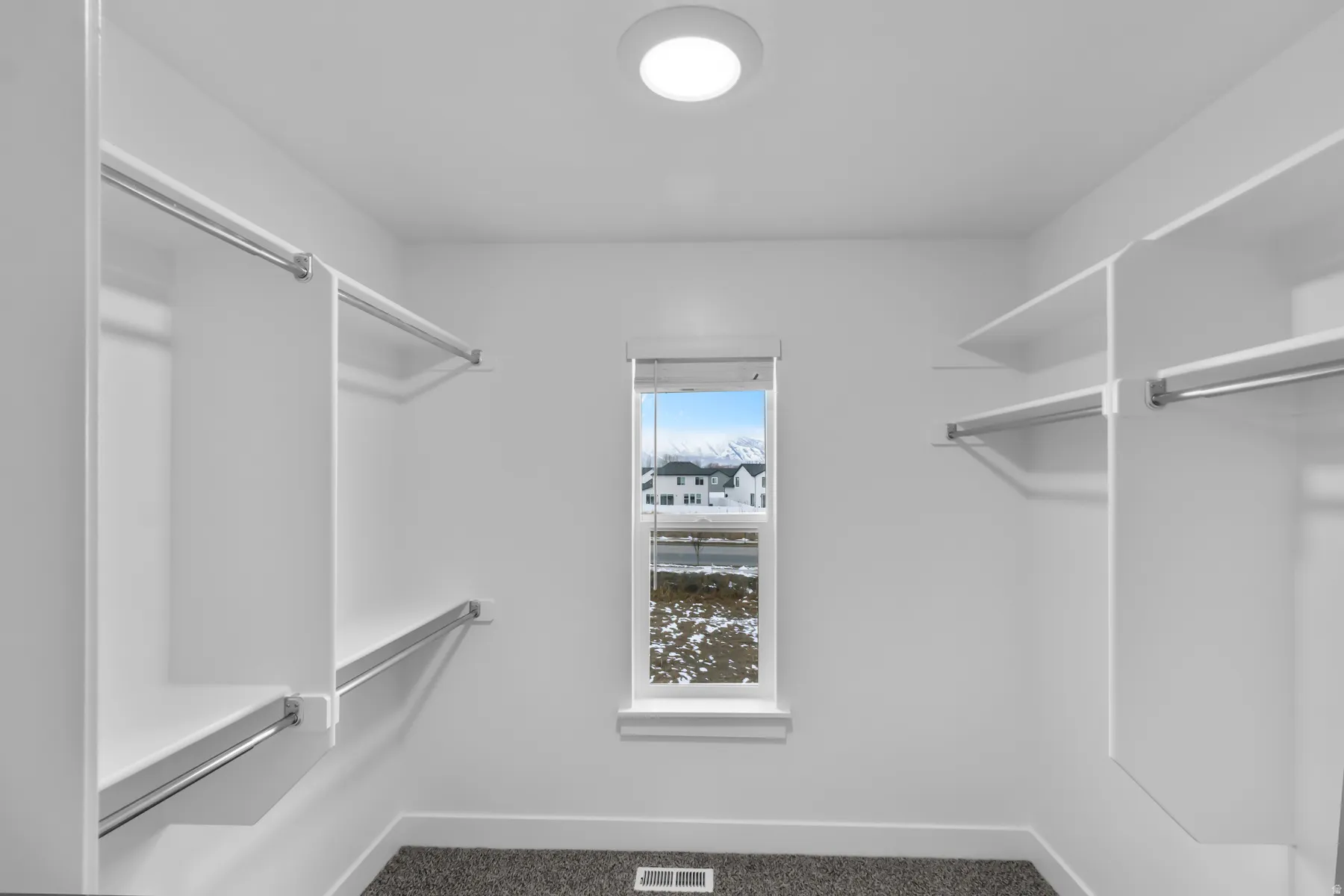 Spacious walk-in closet featuring dual clothing rods with chrome hardware, generous shelving throughout, soft recessed ceiling lighting, and a natural light window with water views