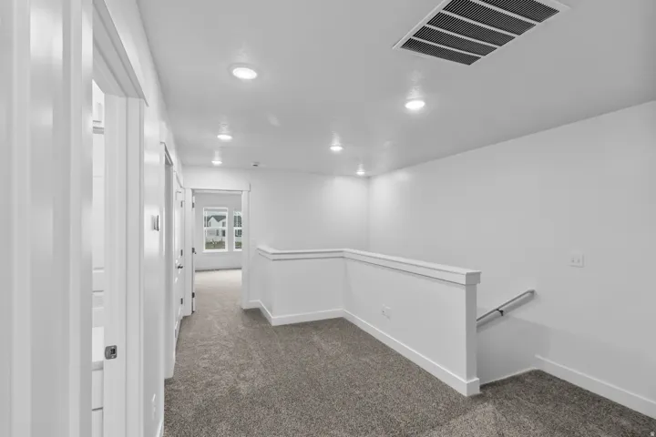 Carpeted hallway with white walls, recessed ceiling lighting, and white railings