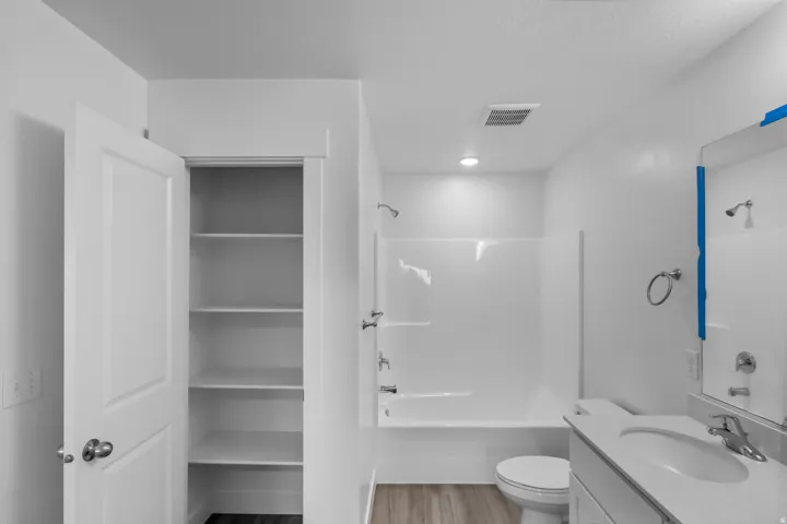 Bathroom featuring a white bathtub, built-in shelving, wood-finish flooring, and a vanity with an integrated sink