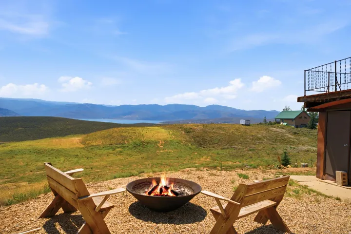 Expansive outdoor entertaining space featuring a built-in fire pit surrounded by wooden Adirondack seating, gravel hardscaping, and panoramic mountain vistas