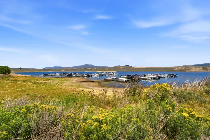 Waterfront setting with a boat dock and multiple vessels, surrounded by rolling hills and natural vegetation