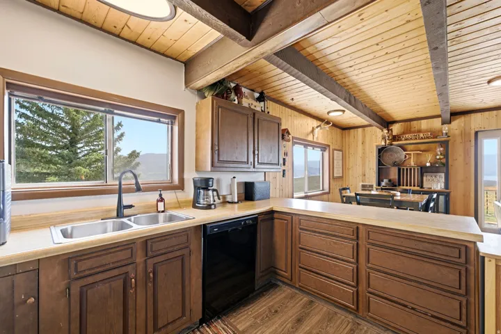 Wood-paneled ceilings with exposed beams, wood-finish flooring, dark wood cabinetry, a dual basin stainless steel sink, and a black dishwasher