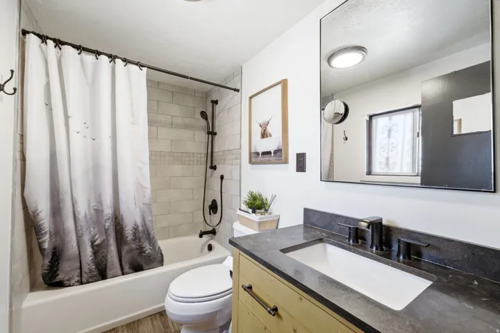 Modern bathroom featuring a wood-finish vanity with dual rectangular vessel sinks, dark stone countertop, and matte black fixtures