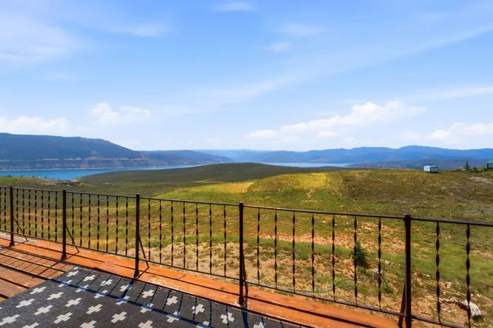 Expansive outdoor deck featuring a wood-finish surface and modern metal railing system, overlooking manicured grounds with panoramic vistas of distant mountains and waterfront landscape