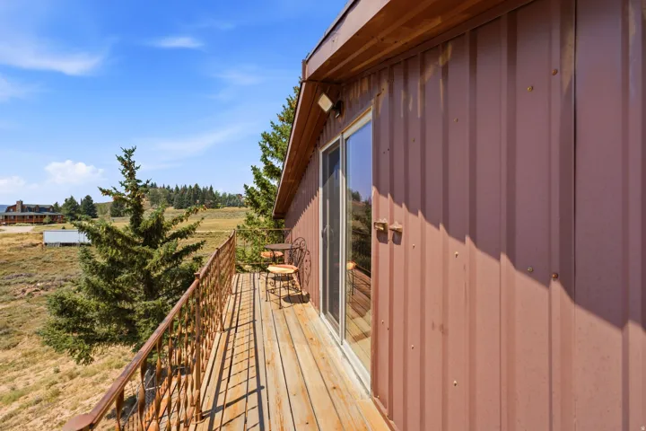 Expansive wooden deck with metal railings overlooking open acreage and evergreen landscaping