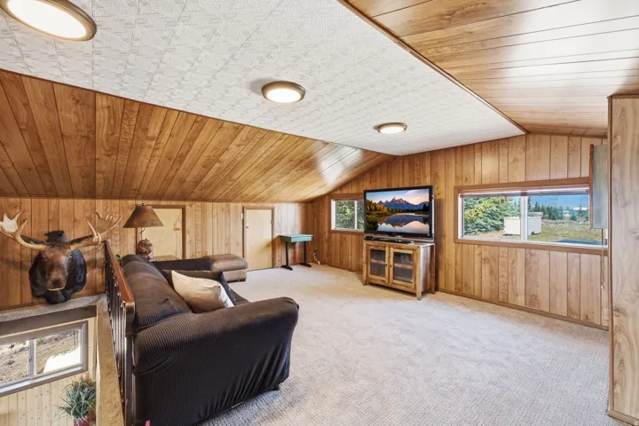 Spacious upper-level recreation room featuring rich wood-paneled walls and ceiling, recessed lighting, wall-mounted entertainment center with cabinetry, and expansive windows offering natural light and scenic outlooks
