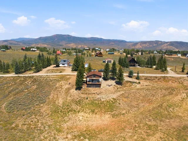 Sprawling rural estate set on expansive grounds with mature evergreen trees, a modern residence featuring wood siding and a covered entry, and panoramic mountain backdrop