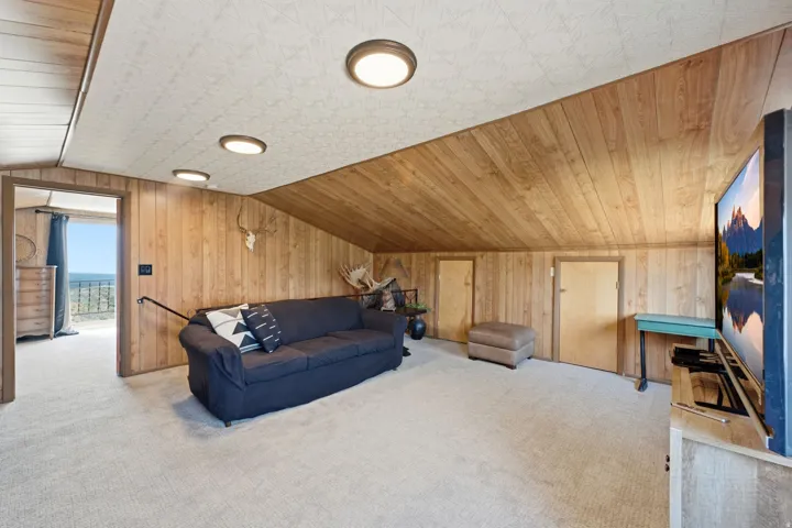 Spacious loft-style room featuring warm wood-finish ceiling and wall paneling, recessed lighting, expansive carpeted flooring, and multiple glass doors opening to outdoor space