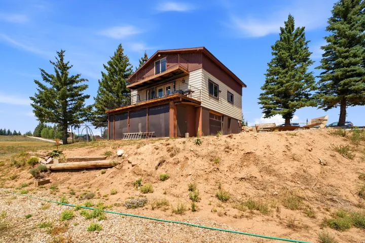 Multi-level residence with warm wood-finish exterior and mixed siding, situated on expansive grounds with mature conifer trees, natural landscaping, and sloped terrain offering elevation and privacy