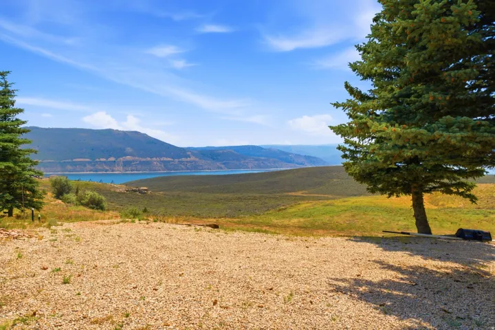 Expansive grounds featuring mature evergreen trees, natural gravel terrain, and panoramic vistas of the surrounding mountainous landscape and distant water features