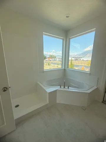 Corner soaking tub with deck-mounted fixtures, separate shower stall, large windows, and light-toned flooring