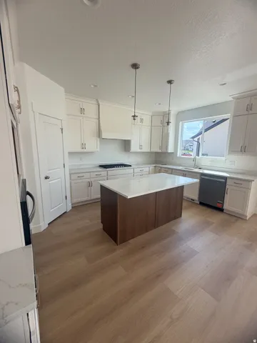 Spacious kitchen featuring an island with a white countertop, wood-finish flooring, white cabinetry, a gas range, and pendant lighting