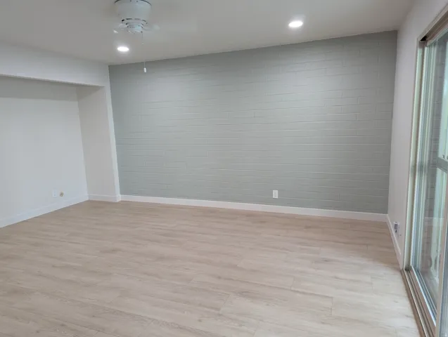 Light wood-finish flooring, recessed lighting, ceiling fan, accent brick wall, and sliding glass door