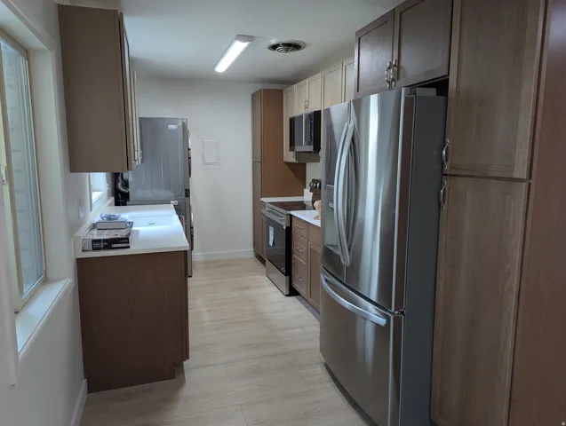 Kitchen featuring wood-finish cabinetry, stainless steel appliances, light countertops, and wood-finish flooring