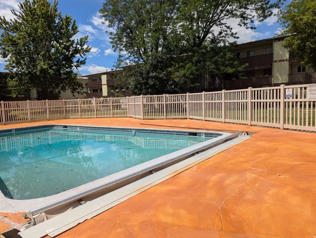 Swimming pool with a light tan picket fence enclosure and expansive orange-toned concrete decking