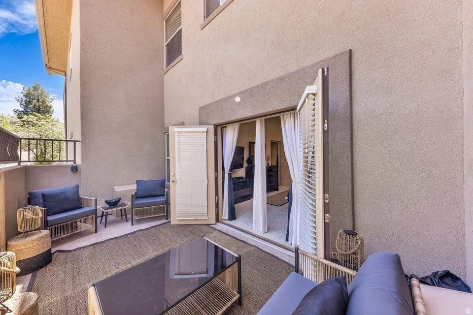 Spacious outdoor living area featuring multiple seating zones, glass sliding doors with white frames opening to the interior, textured area rugs, woven accent tables, and expansive sky views from the elevated terrace with metal railings