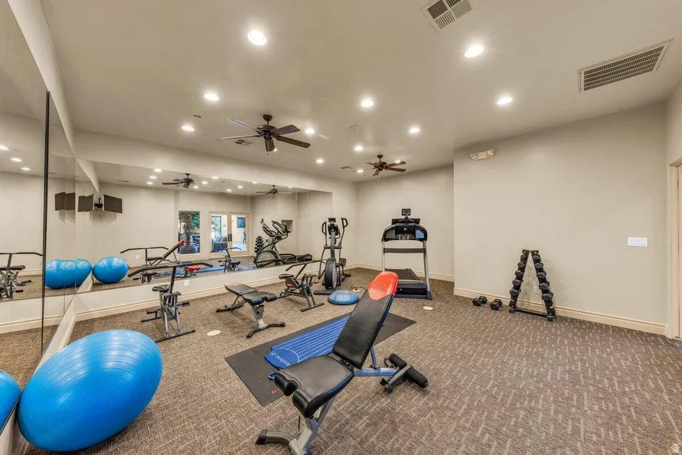 State-of-the-art fitness facility featuring multiple ceiling fans with recessed lighting throughout, mirrored wall systems for form feedback, durable textured flooring, and an array of exercise equipment including cardio machines, weight benches, and stab