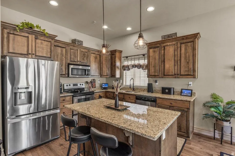 Kitchen featuring wood-finish cabinetry, stainless steel appliances, a granite-topped island, and recessed lighting