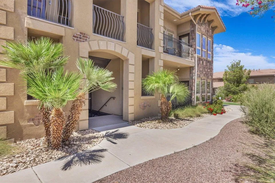 Stucco exterior with stone accents, wrought iron balcony railings, arched entryways, and mature landscaping