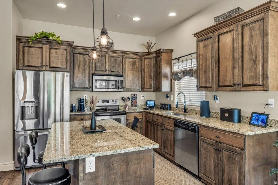 Chef's kitchen featuring custom wood-finish cabinetry, granite countertops, stainless steel appliances, a large center island with seating, and pendant lighting over the workspace