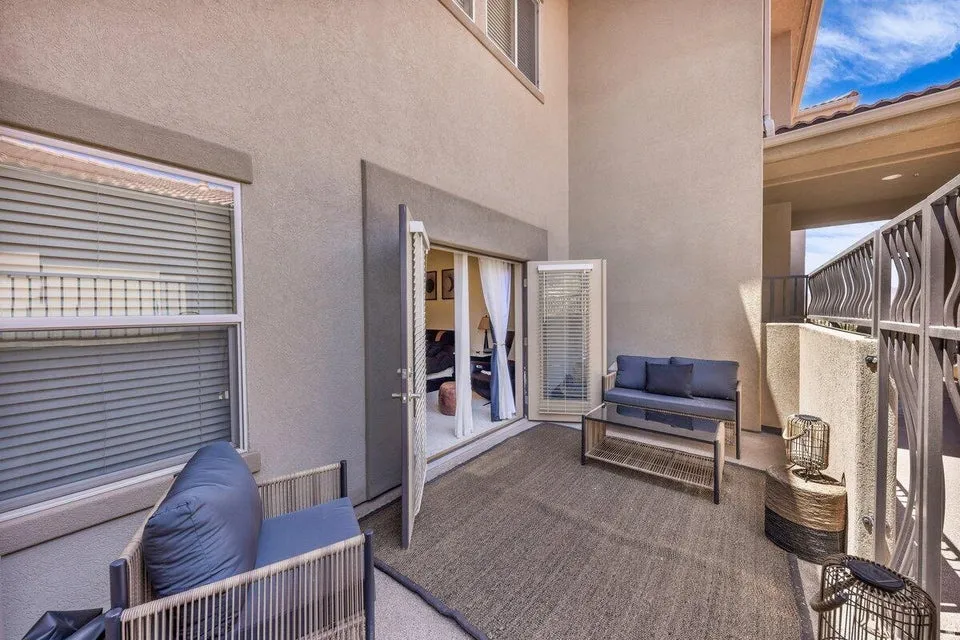Bright, open-air patio space featuring neutral-toned textured flooring, built-in seating with blue cushioning, mirrored closet doors with louvered ventilation, roller shades on adjacent windows, and abundant natural light from multiple glass sliding doors