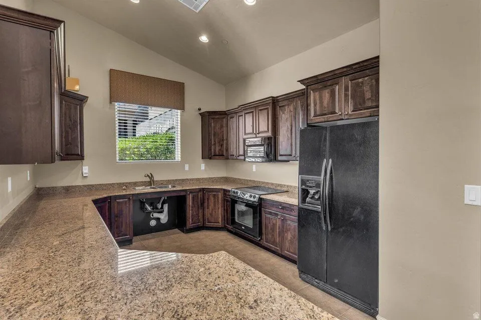 Kitchen featuring U-shaped stone-finish countertops, dark wood cabinetry, and a black appliance suite