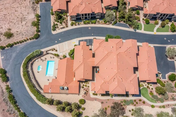 Multi-unit residential property with terracotta-style roofs, a curvilinear asphalt driveway, a rectangular swimming pool, and an integrated spa