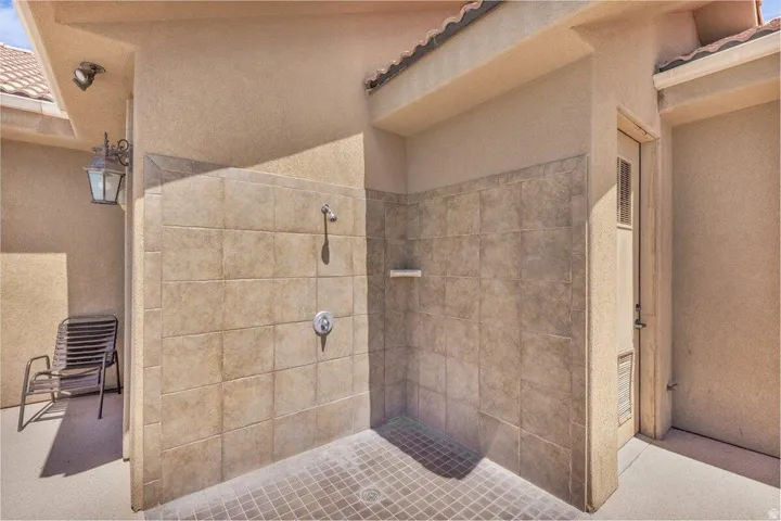 Spa-inspired primary bathroom featuring a frameless glass shower enclosure with dual showerheads, neutral tile surround, and a dark tile floor with radiant heating