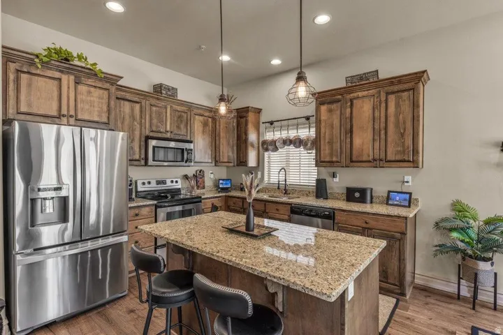 Kitchen featuring wood-finish cabinetry, stainless steel appliances, a granite-topped island, and recessed lighting