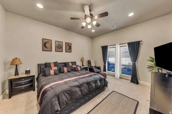 Spacious primary bedroom suite featuring recessed ceiling lighting, ceiling fan with integrated light fixture, dual nightstands with wood-finish surfaces, and glass sliding doors opening to a private balcony
