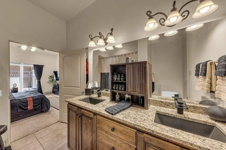 Spa-inspired primary bathroom featuring dual vanities with wood-finish cabinetry, light stone countertops, and undermount sinks