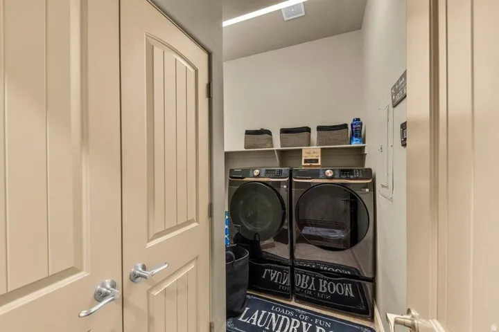 Dedicated laundry room featuring side-by-side front-load washer and dryer with overhead storage shelving, neutral cabinetry, and recessed ceiling lighting for optimal functionality