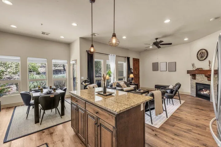Open-concept living area with wood-finish flooring, a stone-faced fireplace with a wood mantle, and a kitchen island with a granite countertop