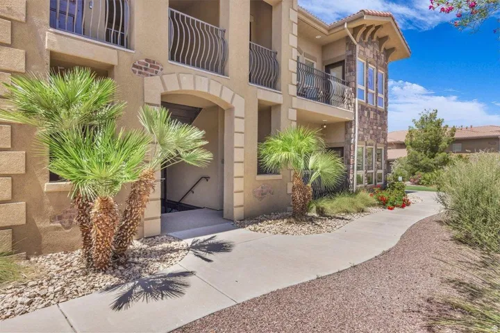 Stucco exterior with stone accents, wrought iron balcony railings, arched entryways, and mature landscaping