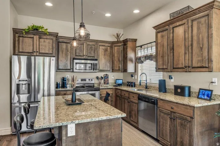 Chef's kitchen featuring custom wood-finish cabinetry, granite countertops, stainless steel appliances, a large center island with seating, and pendant lighting over the workspace