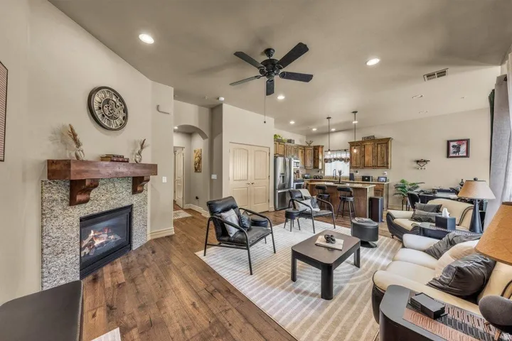 Open-concept living space featuring wood-finish flooring, a corner fireplace with a granite surround, and a ceiling fan